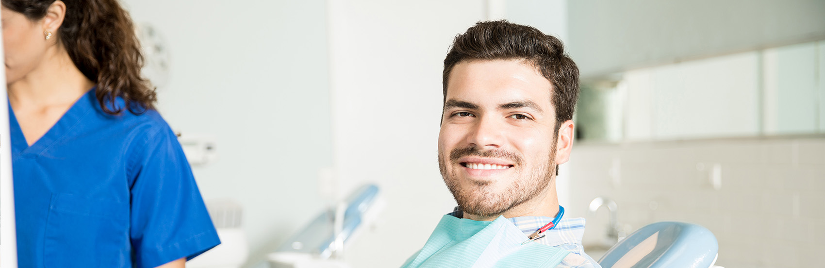 Hispanic man in dental chair turning his head to the side to smile at the camera, dentist in haymarket