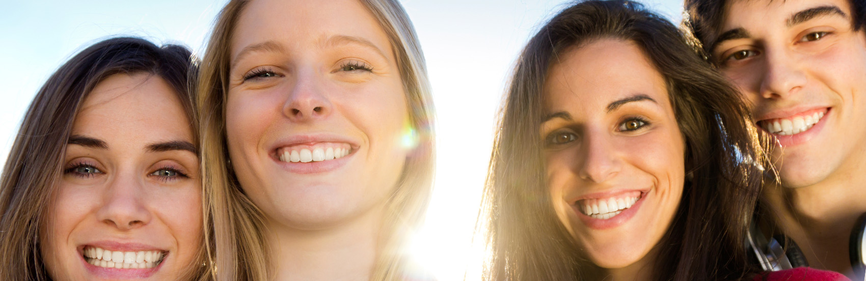 four young people smiling while the sun shines behind them